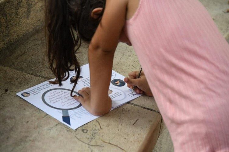 Enfant en train de dessiner sur une feuille en extérieur. rallye-decouverte